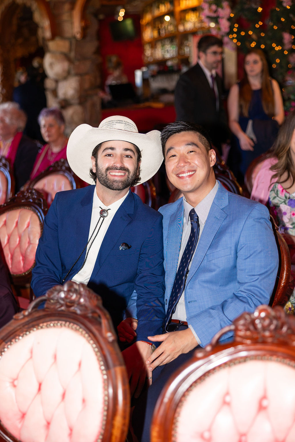 Wedding guests in blue smile while sitting in pink vintage chairs