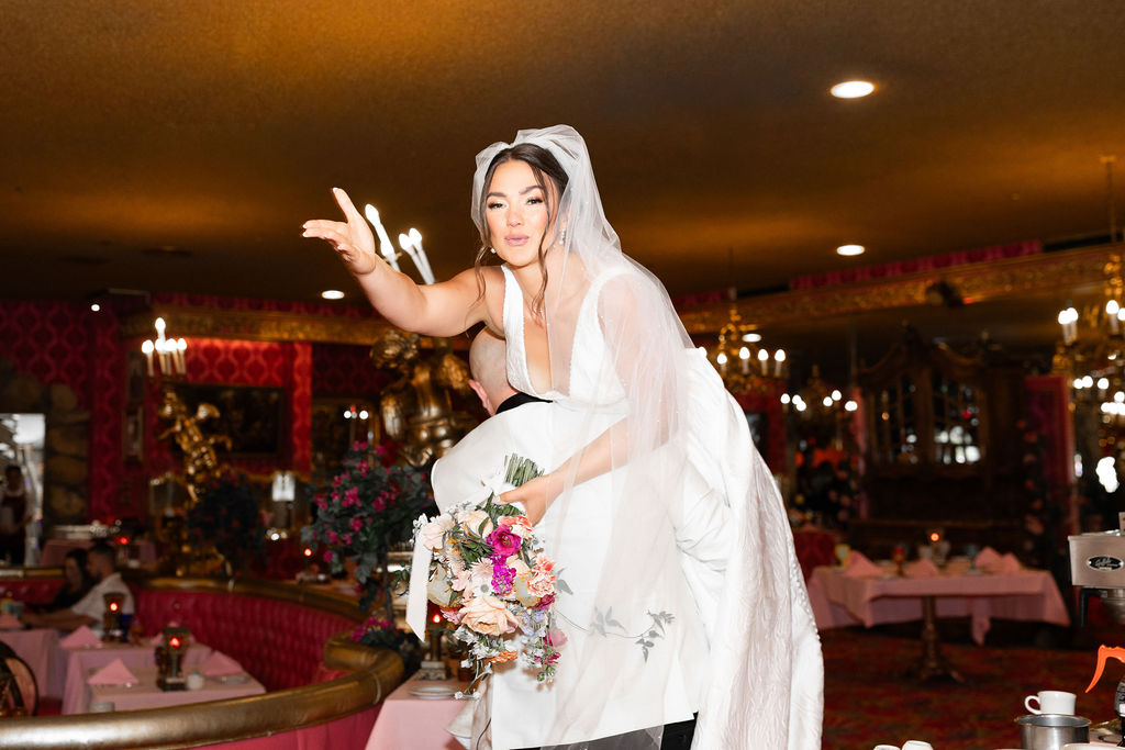 A bride is carried by her groom through their Madonna Inn wedding reception over his shoudler