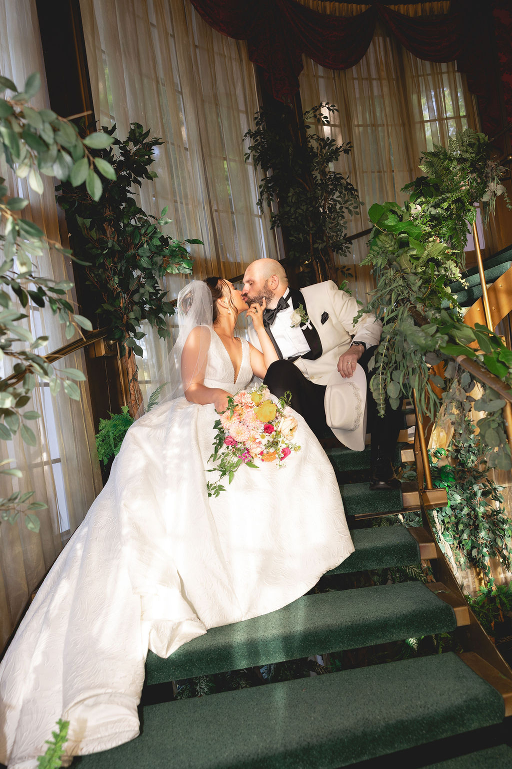 Newlyweds sit on grand gold staircase kissing at the Madonna Inn wedding venue