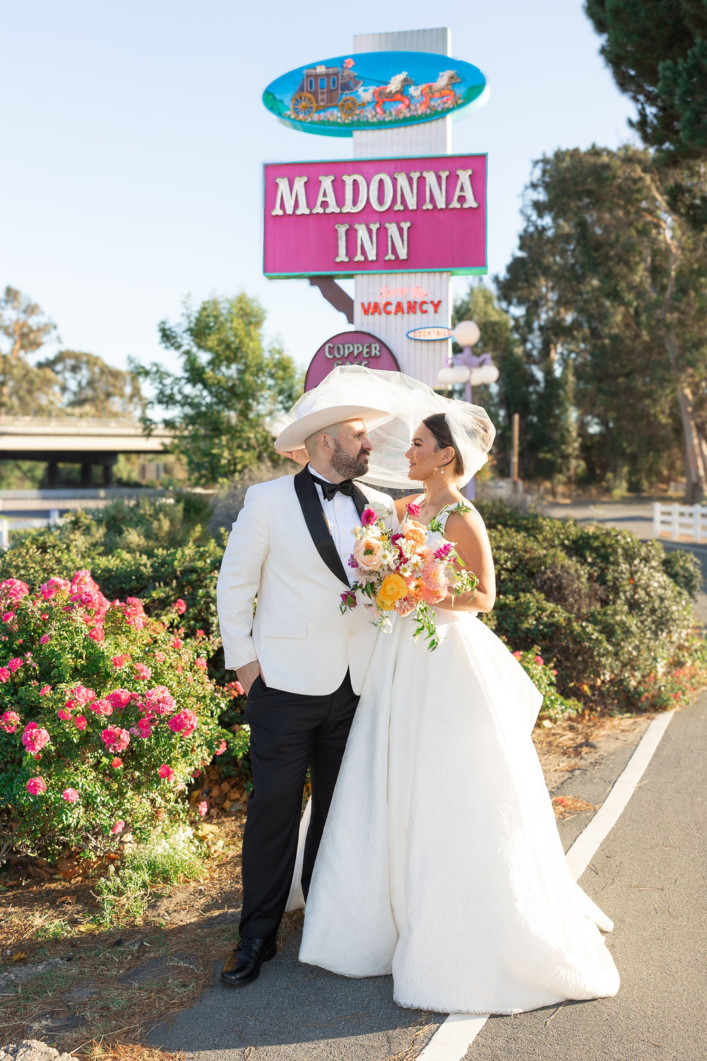 Newlyweds stand smiling at each other under the Madonna Inn wedding venue sign