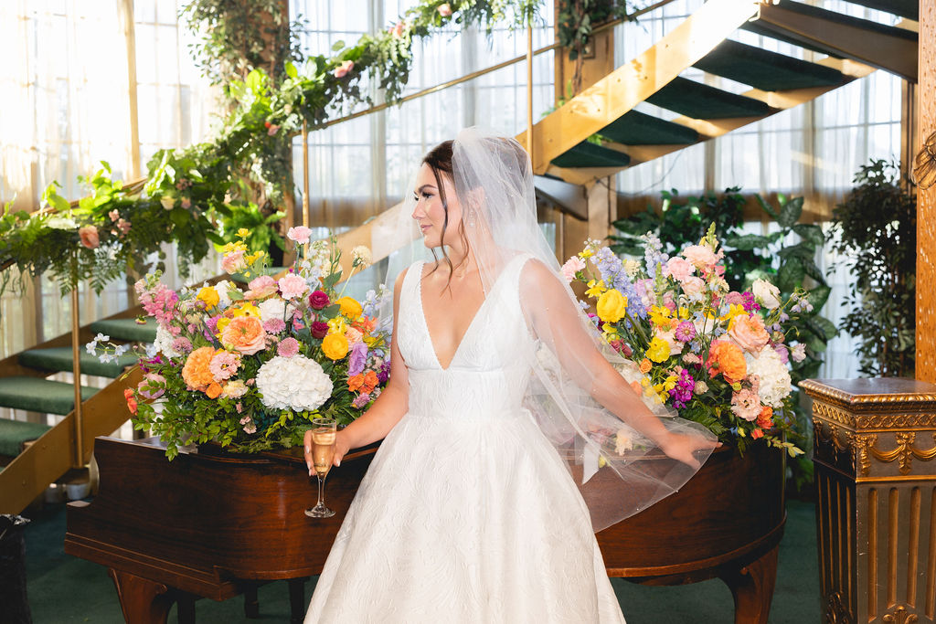 A bride lounges across a piano in the Madonna Inn wedding venue lobby with a glass of champagne