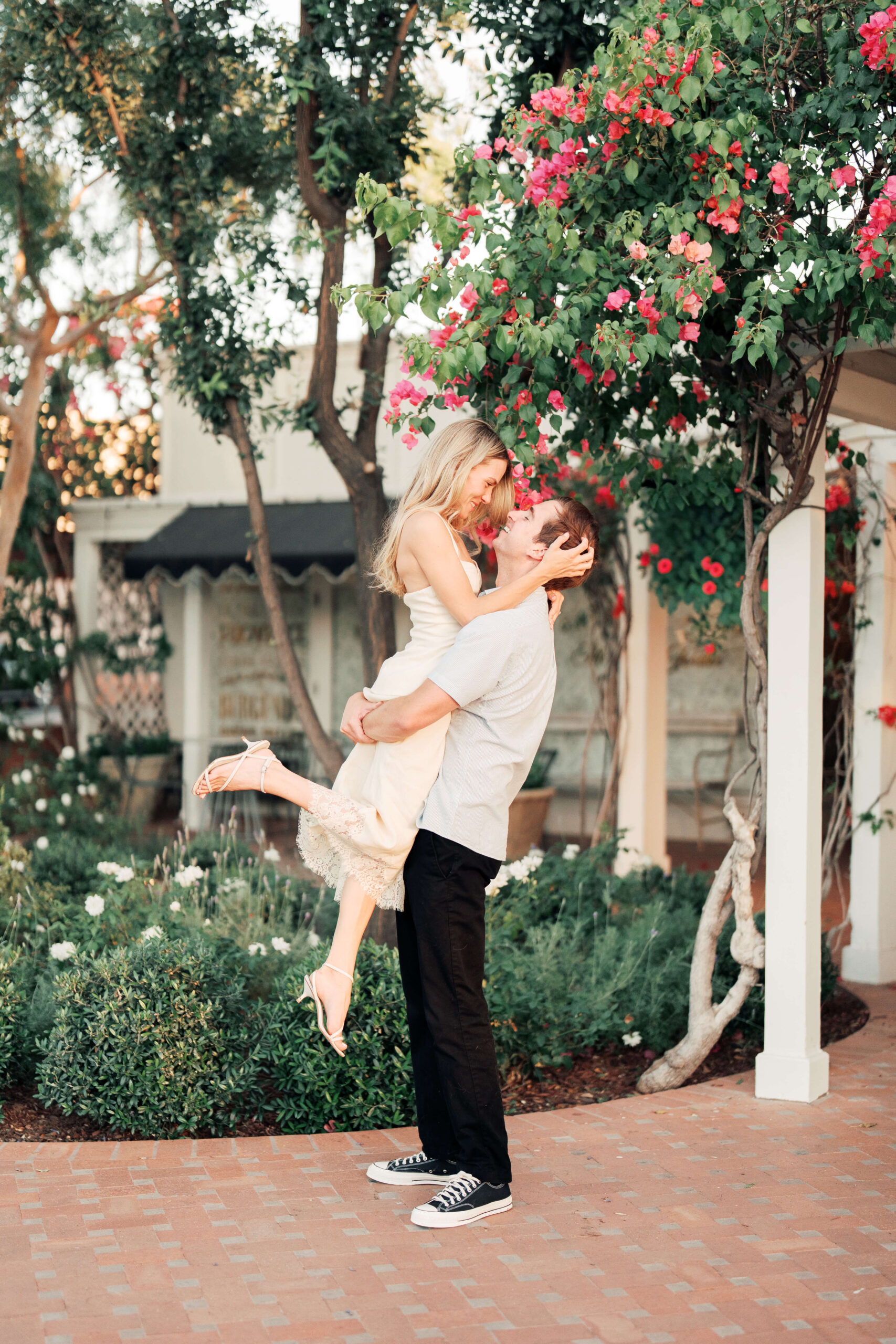 Bride is lifted up by groom for the engagement photos surrounded by greenery