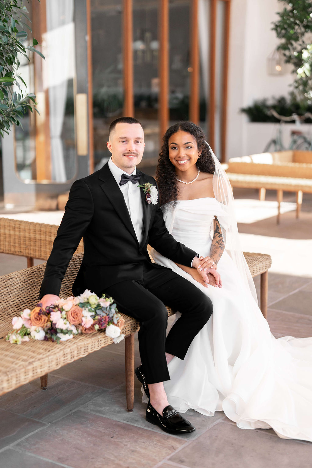 Happy newlyweds sit on a wicker bench smiling on a patio during their day at the scott resort wedding venue