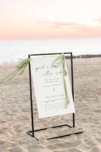 A wedding welcome sign blows in the wind on the beach