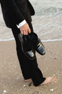 Details of a grooms suit and shoes while standing on the beach