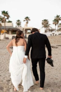 Couple lovingly looks at each other while walking hand in hand on the beach for bridal portraits
