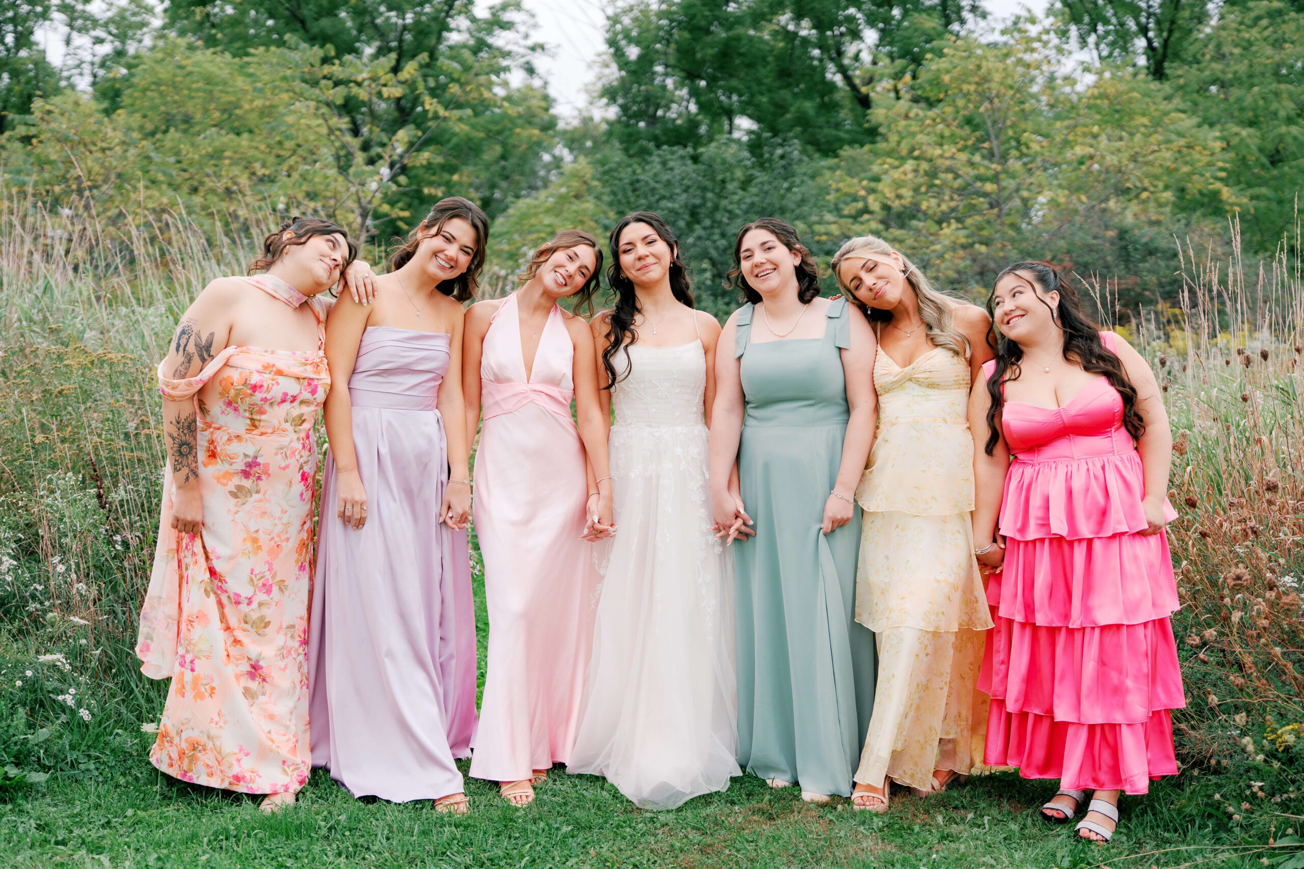 A bridal party with colorful dresses pose with the bride surrounded by greenery
